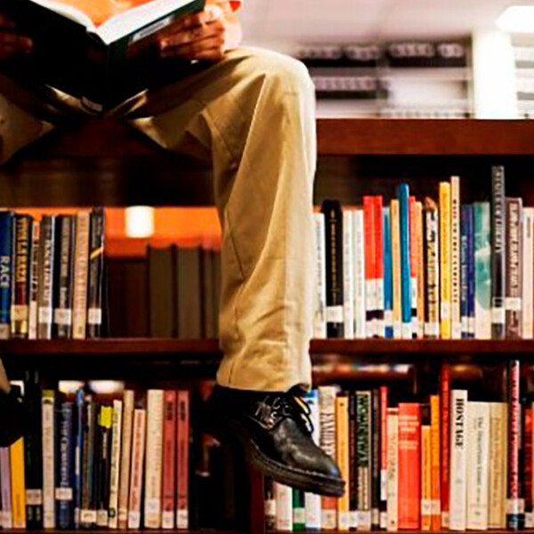 Man sitting on library shelf reading book.