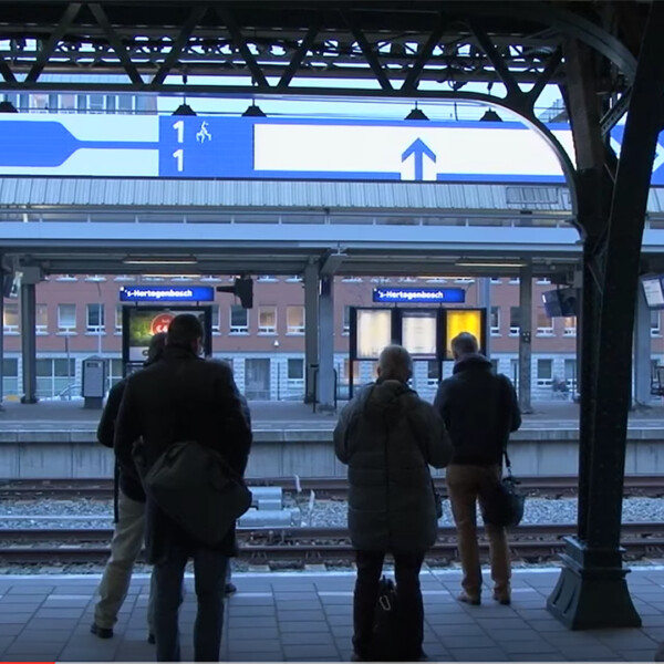 People waiting on a train platform, looking at a large screen with info about the composition of the train.
